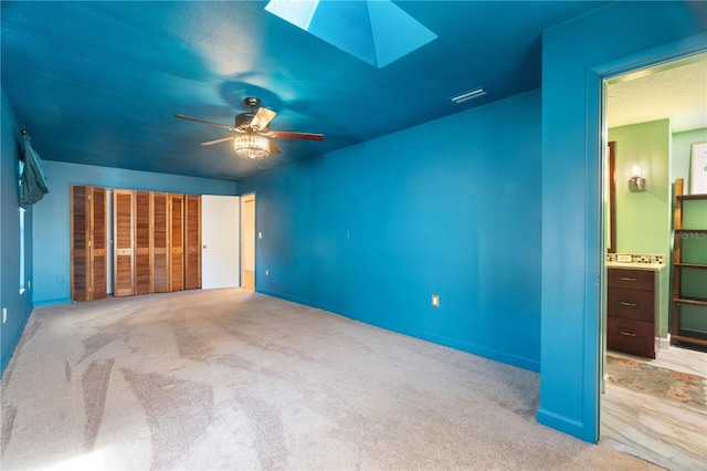 unfurnished bedroom featuring carpet flooring, a ceiling fan, a skylight, and connected bathroom