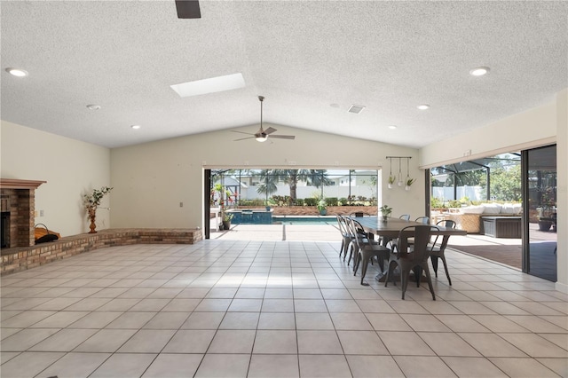 dining space featuring a textured ceiling, a brick fireplace, ceiling fan, and vaulted ceiling with skylight