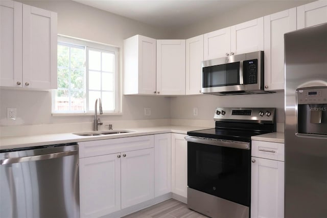 kitchen with light countertops, white cabinetry, stainless steel appliances, light wood finished floors, and a sink