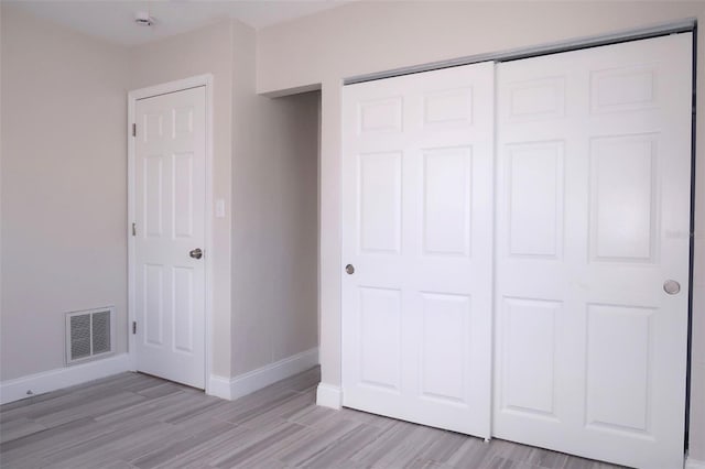 unfurnished bedroom featuring light wood-style floors, a closet, baseboards, and visible vents