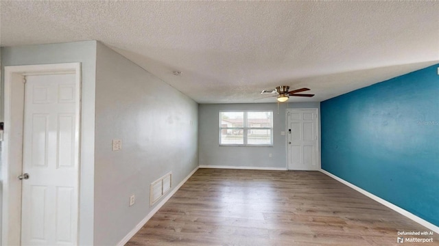 empty room with a textured ceiling, visible vents, baseboards, ceiling fan, and wood finished floors