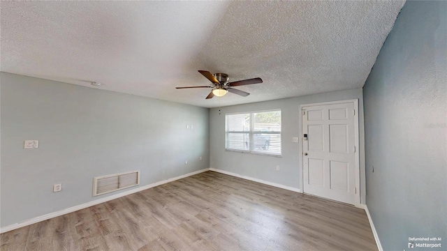 spare room featuring a textured ceiling, visible vents, baseboards, a ceiling fan, and light wood-type flooring