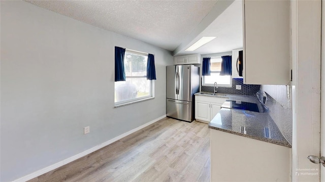 kitchen featuring light wood-type flooring, baseboards, a textured ceiling, backsplash, and freestanding refrigerator