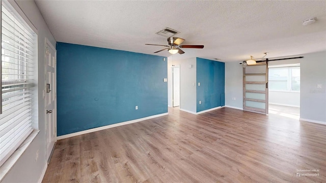 empty room featuring visible vents, wood finished floors, ceiling fan, and a textured ceiling