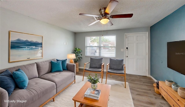 living room with a ceiling fan, baseboards, light wood-style floors, and a textured ceiling