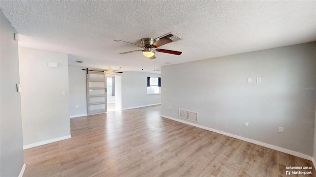 empty room featuring light wood-style flooring, visible vents, baseboards, a ceiling fan, and a barn door