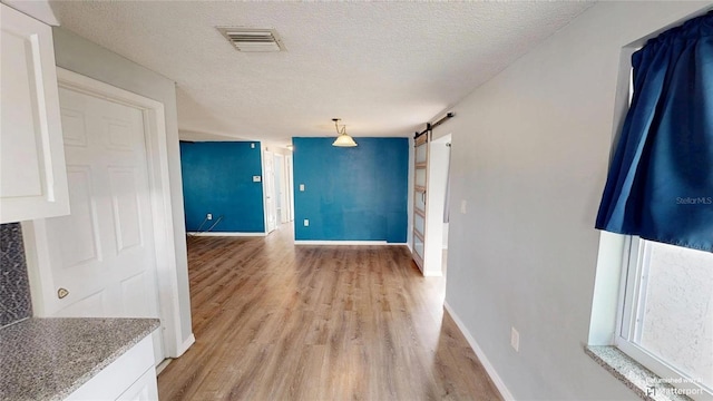 interior space with light wood-style floors, a textured ceiling, a barn door, and visible vents