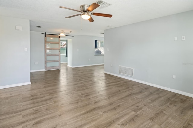 spare room with a barn door, ceiling fan, visible vents, and wood finished floors