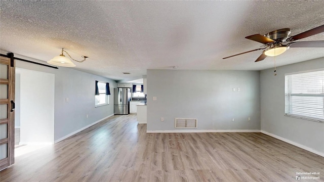interior space with visible vents, a barn door, ceiling fan, and light wood-type flooring