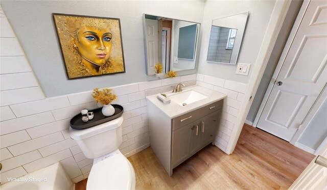 bathroom featuring toilet, vanity, wood finished floors, wainscoting, and tile walls