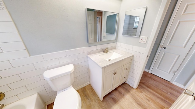 bathroom featuring a wainscoted wall, toilet, vanity, wood finished floors, and tile walls