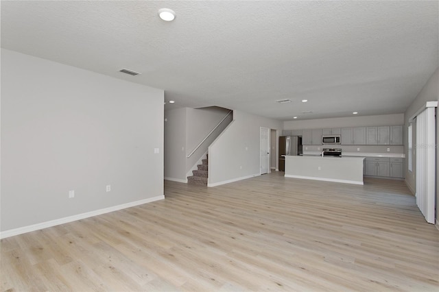 unfurnished living room featuring stairs, a textured ceiling, light wood-style flooring, baseboards, and visible vents