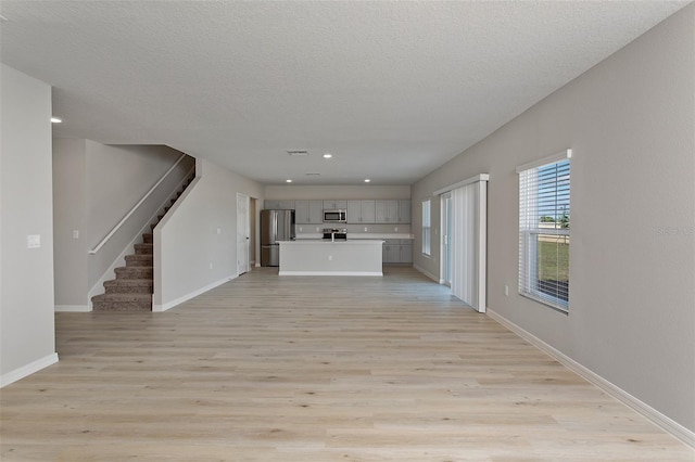 unfurnished living room featuring baseboards, a textured ceiling, light wood-style flooring, and stairway