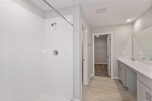 bathroom featuring vanity, a walk in closet, a tile shower, baseboards, and wood finished floors