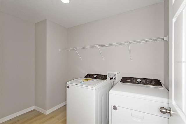 clothes washing area with baseboards, laundry area, separate washer and dryer, and light wood-type flooring