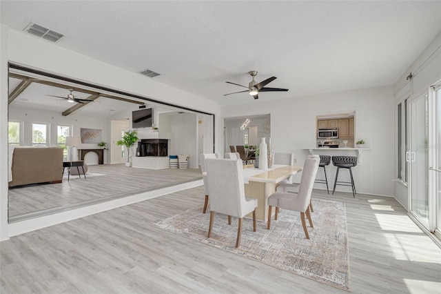 7906 Bayshore Dr, Seminole, FL 33776 - dining area featuring light wood-style flooring, visible vents, ceiling fan, and a fireplace