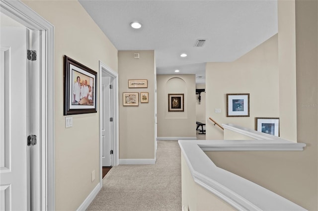 hall with an upstairs landing, carpet floors, baseboards, visible vents, and recessed lighting