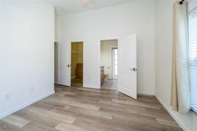 5331 Villagebrook Dr, Wesley Chapel, FL 33544 - unfurnished bedroom featuring light wood-style flooring, a spacious closet, ensuite bath, baseboards, and a high ceiling