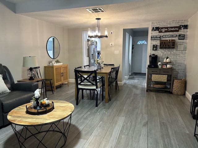 dining space featuring an inviting chandelier, a textured ceiling, visible vents, wood finished floors, and baseboards