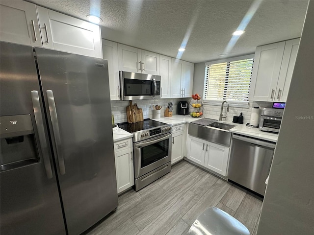 kitchen featuring white cabinets, light countertops, appliances with stainless steel finishes, wood tiled floor, and decorative backsplash