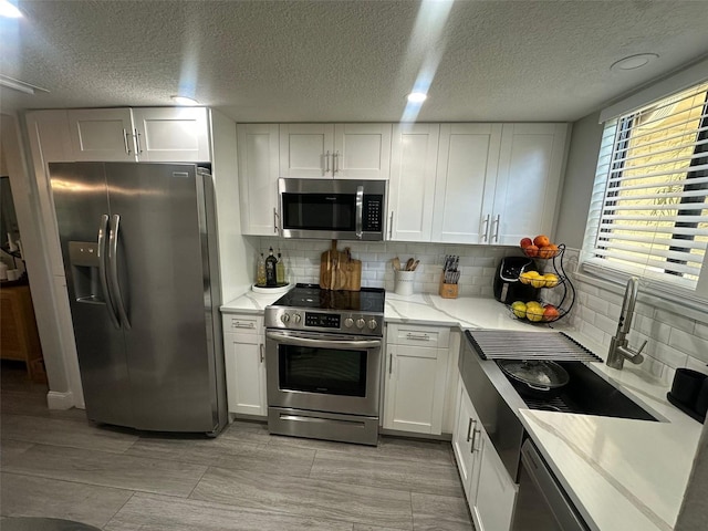 kitchen featuring tasteful backsplash, white cabinetry, a sink, and appliances with stainless steel finishes