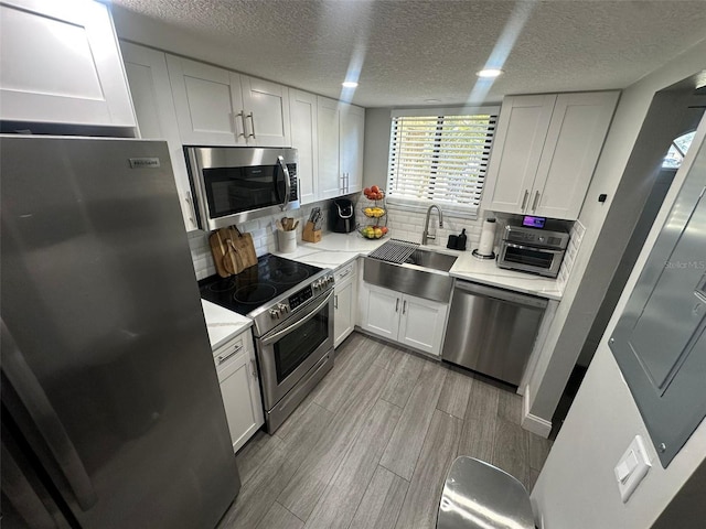 kitchen featuring white cabinets, a sink, wood finish floors, stainless steel appliances, and decorative backsplash