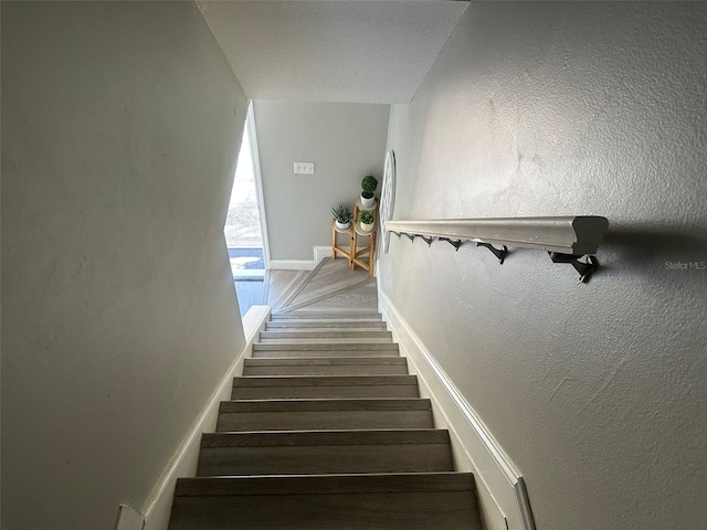 staircase featuring baseboards, wood finished floors, and a textured wall