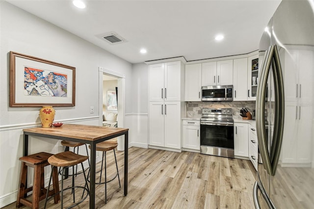 610 N Woodlynne Ave, Tampa, FL 33609 - kitchen featuring light countertops, backsplash, appliances with stainless steel finishes, light wood-style flooring, and white cabinets