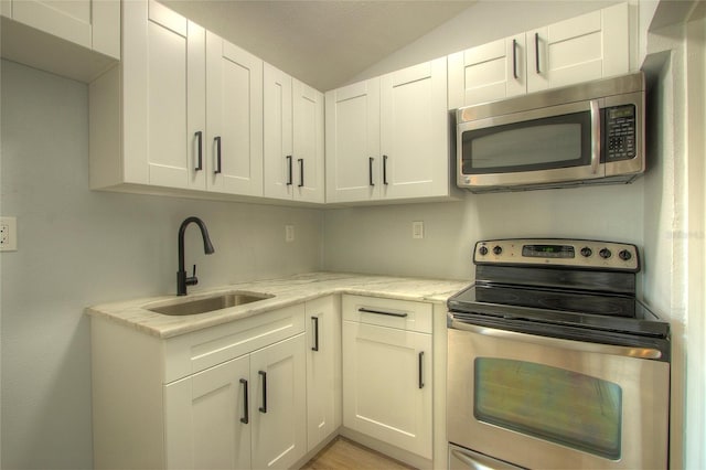 610 N Woodlynne Ave, Tampa, FL 33609 - kitchen featuring white cabinets, stainless steel appliances, a sink, light stone counters, and vaulted ceiling