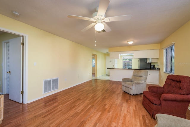 living area with light wood finished floors, baseboards, visible vents, and a ceiling fan