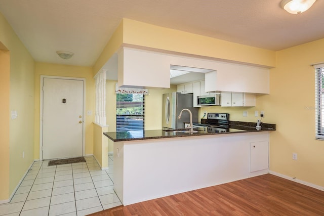 kitchen featuring a sink, a peninsula, dark stone countertops, stainless steel appliances, and white cabinets