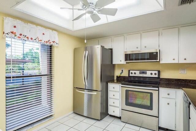 kitchen featuring light tile patterned flooring, a ceiling fan, appliances with stainless steel finishes, dark countertops, and white cabinets
