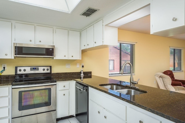kitchen featuring visible vents, dark stone counters, appliances with stainless steel finishes, white cabinetry, and a sink