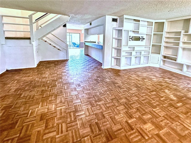 unfurnished living room with a textured ceiling, visible vents, and stairs