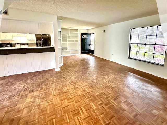 unfurnished living room with a textured ceiling, visible vents, baseboards, and a sink