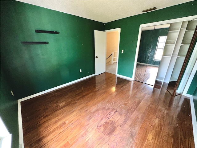 unfurnished bedroom with a closet, baseboards, visible vents, and wood finished floors