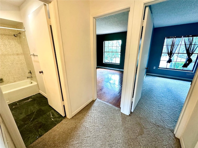 hall with a textured ceiling, carpet flooring, and baseboards