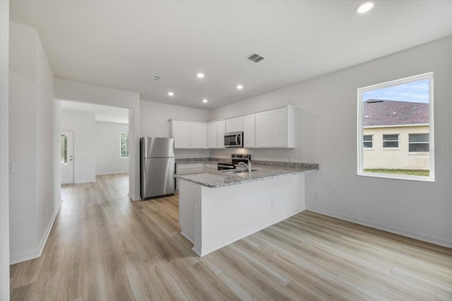 385 Begonia Ct, Poinciana, FL 34759 - kitchen featuring appliances with stainless steel finishes, a peninsula, light stone counters, light wood-style flooring, and white cabinets