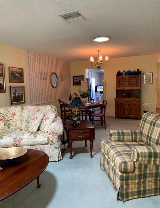 living room with wallpapered walls, a chandelier, light carpet, a textured ceiling, and visible vents