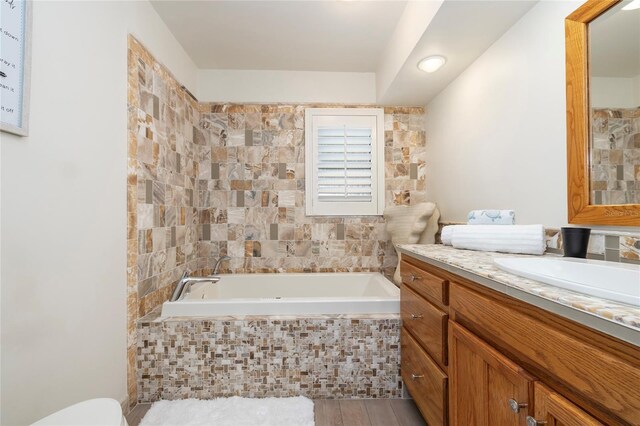 bathroom with tiled tub, vanity, wood finished floors, and toilet