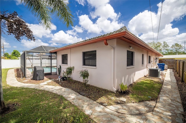 view of side of home with a fenced backyard, cooling unit, stucco siding, a swimming pool, and glass enclosure