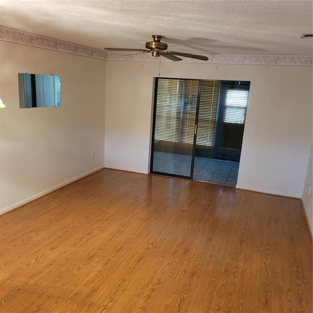 empty room with a textured ceiling, baseboards, ceiling fan, and wood finished floors