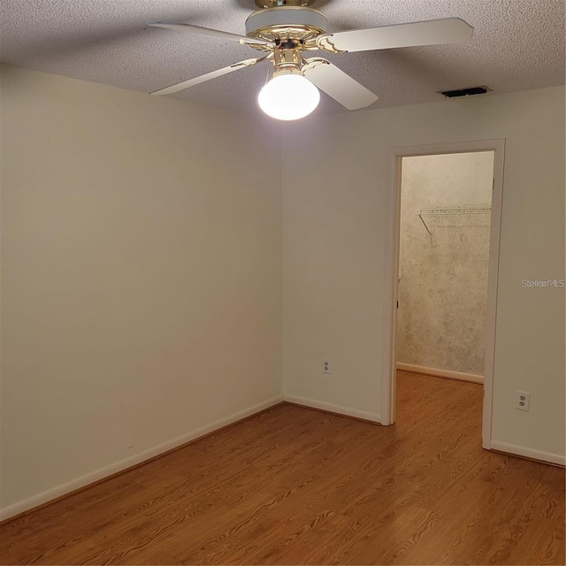 spare room featuring a textured ceiling, visible vents, baseboards, a ceiling fan, and light wood-type flooring