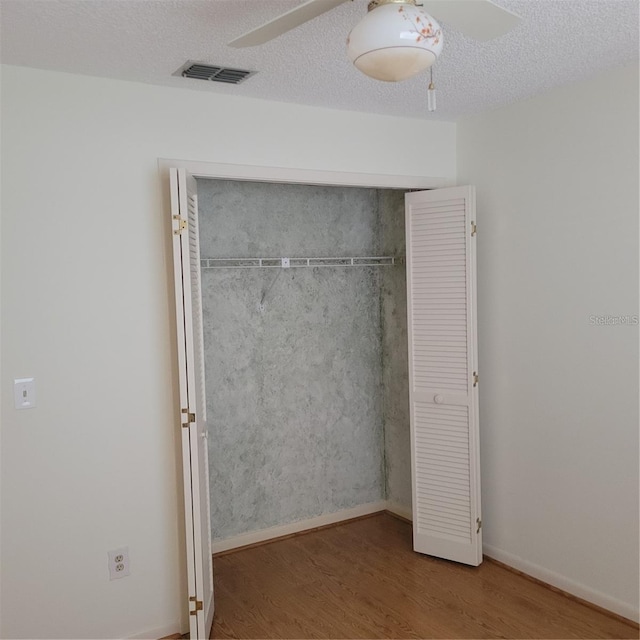unfurnished bedroom featuring a textured ceiling, ceiling fan, visible vents, a closet, and wood finished floors