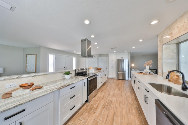 kitchen featuring island range hood, a sink, light wood-style floors, white cabinets, and appliances with stainless steel finishes