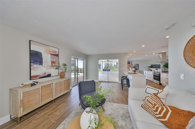 living area with a textured ceiling, baseboards, ceiling fan, wood finished floors, and recessed lighting