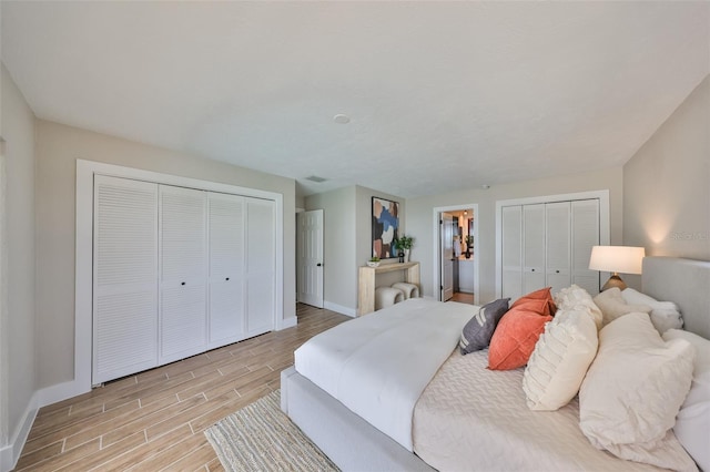 bedroom with two closets, baseboards, and wood tiled floor
