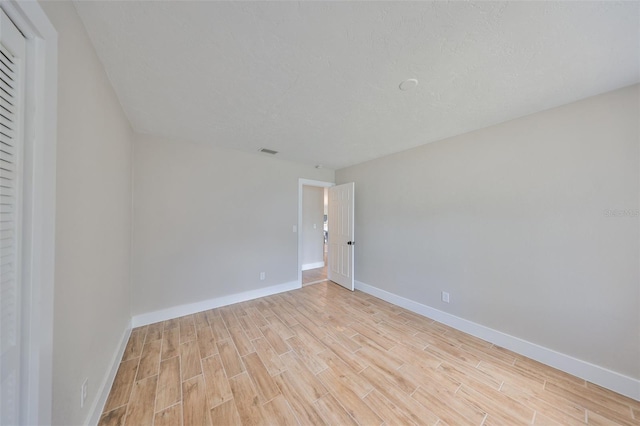spare room with visible vents, a textured ceiling, baseboards, and light wood-type flooring