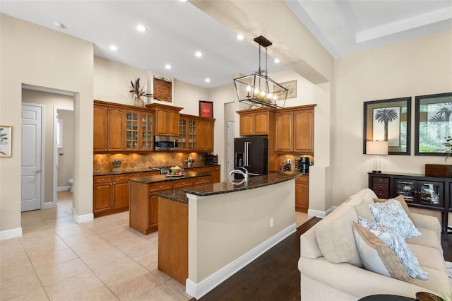 14817 Tudor Chase Dr, Tampa, FL 33626 - kitchen featuring high quality fridge, a center island with sink, brown cabinets, backsplash, and dark stone counters