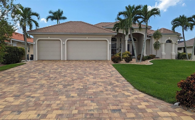mediterranean / spanish-style house featuring a tiled roof, decorative driveway, a garage, a front lawn, and stucco siding